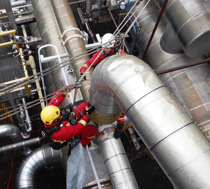 A technician performing rope access insulation work on piping, suspended from ropes in an industrial setting, demonstrating precision and safety in a high-access area.